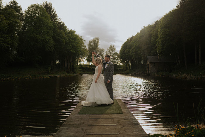 A Bride And Groom Pose And Groom Twirls Bride On A Wooden Pier Surrounded By Water