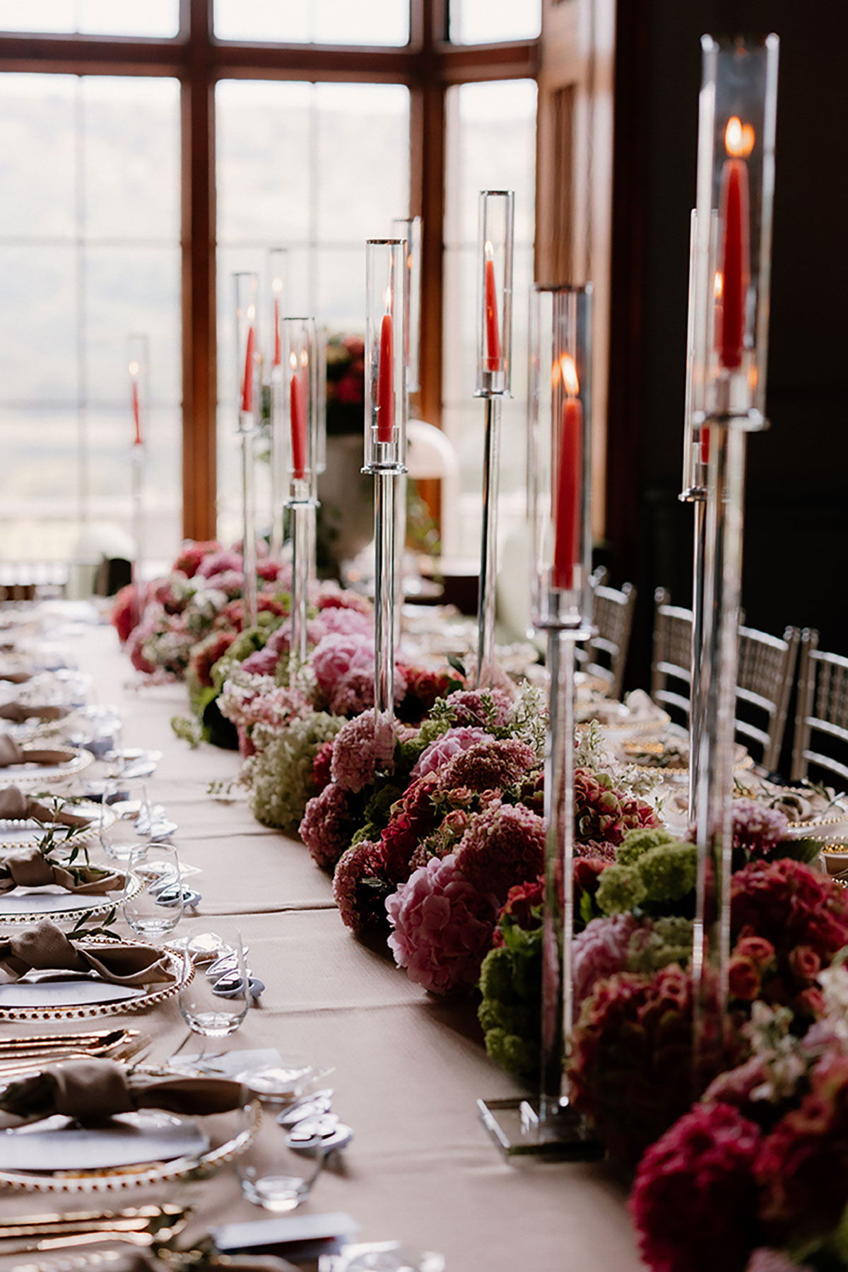 Close-up of tall red candles and lush floral arrangements along the wedding reception table at Mar Hall.