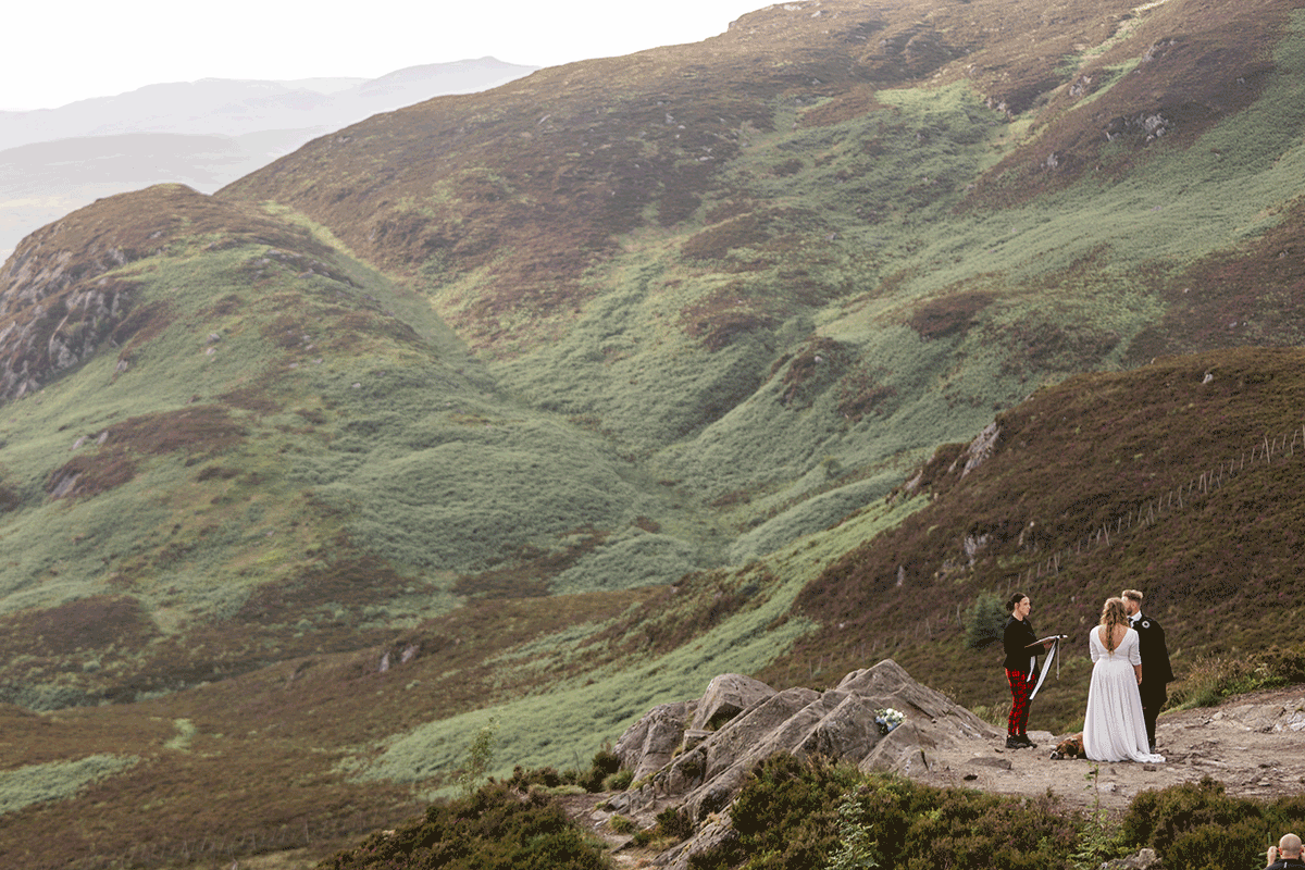 Wide view of a remote Scottish elopement ceremony on a rocky outcrop surrounded by sweeping Highland hills and dramatic natural scenery