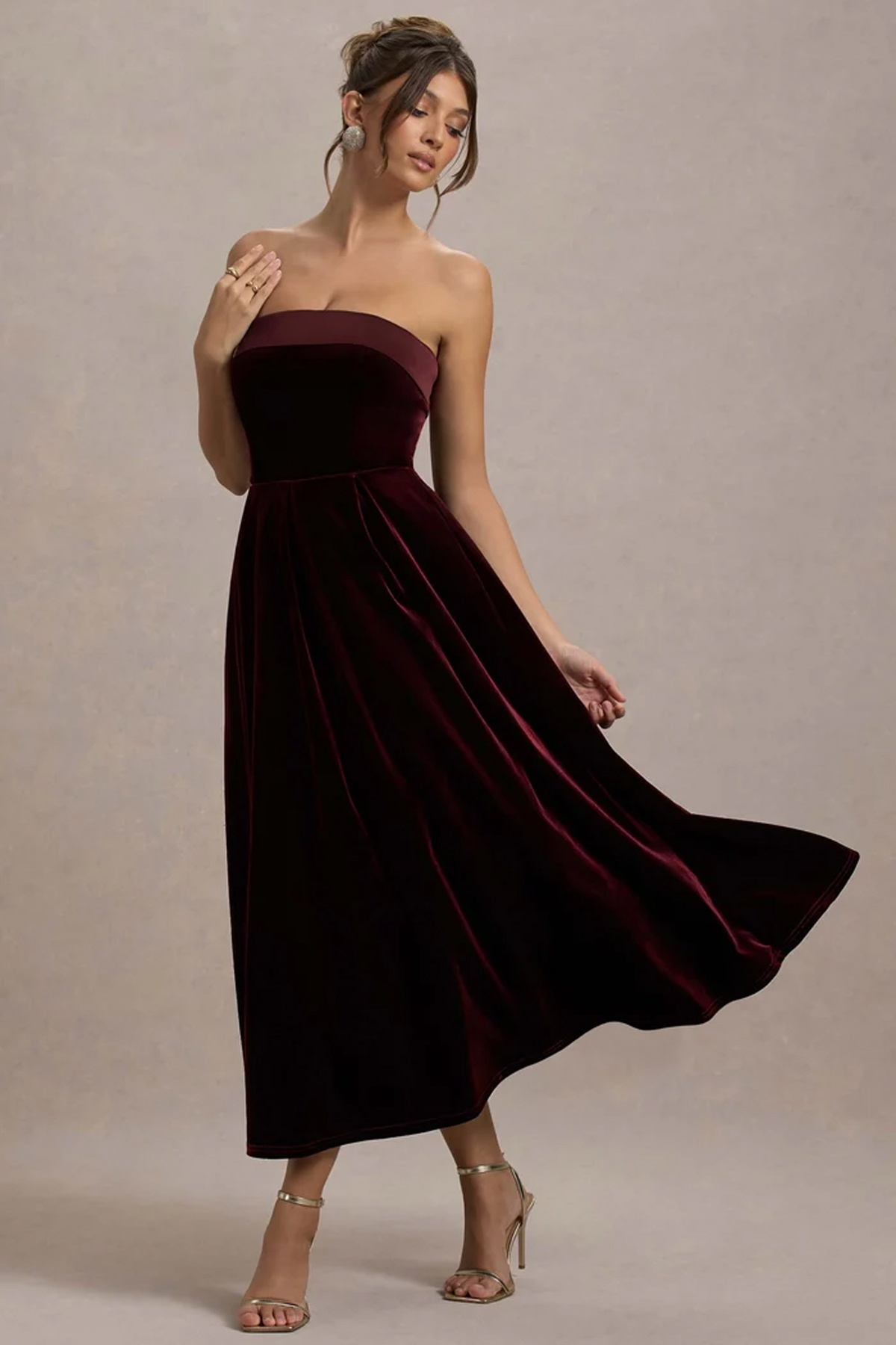 Woman wearing a burgundy velvet bandeau midi dress with a fitted bodice and full flowing skirt.