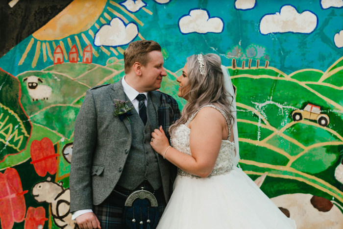 A Bride And Groom Standing Against A Colourful Mural