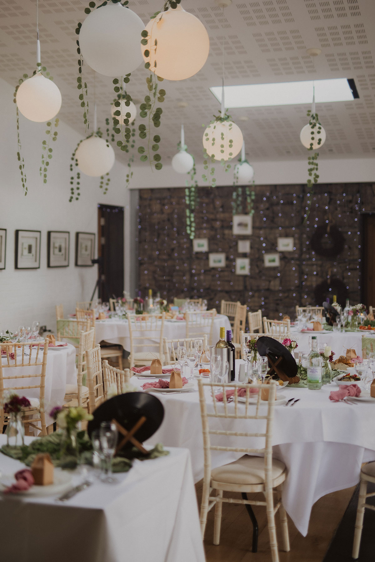 Wedding reception tables styled with white linens, gold Chiavari chairs and hanging globe lights with greenery at modern Scottish venue