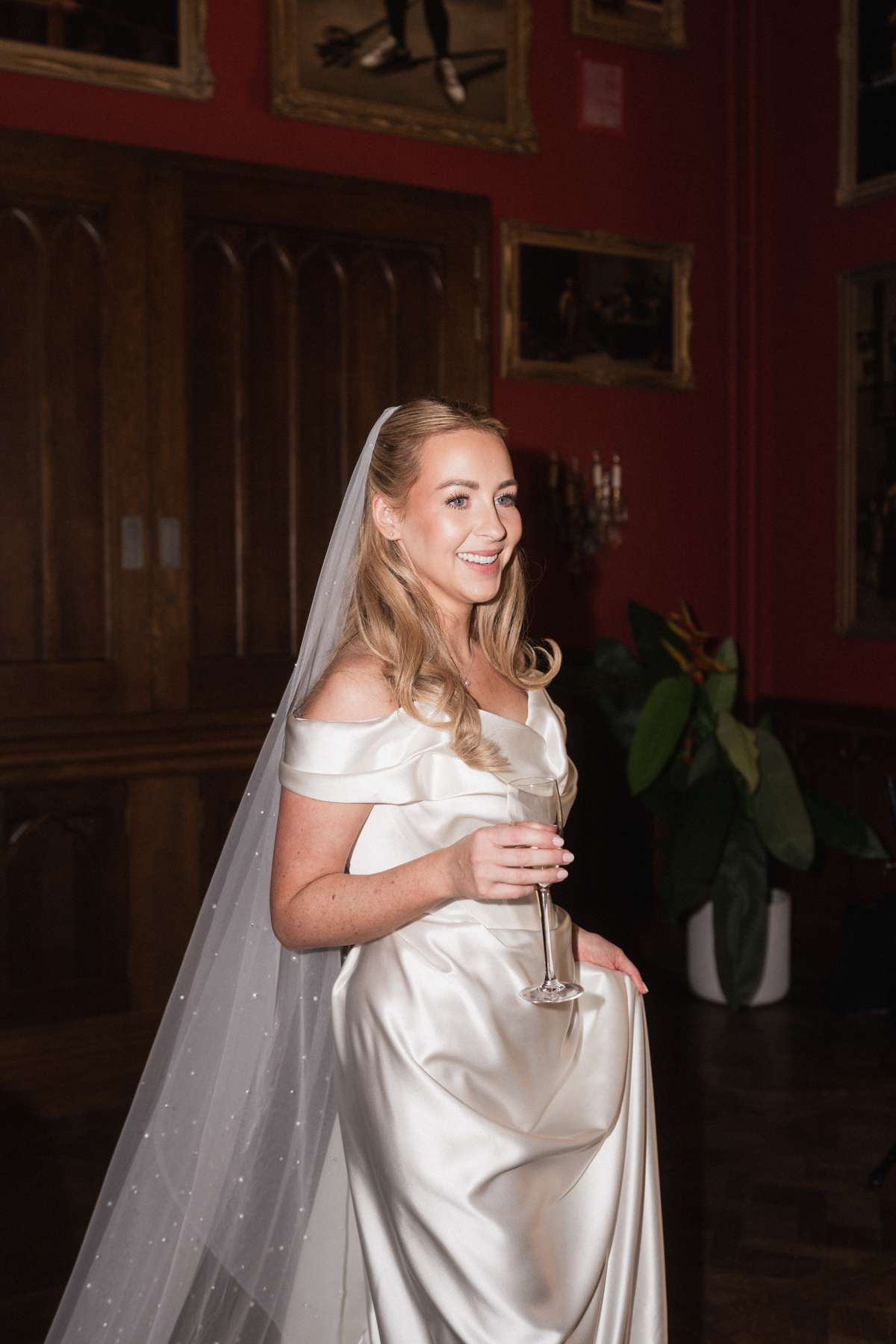 Bride Siân smiles with a glass of champagne in her Vivienne Westwood wedding dress and veil at Mar Hall.