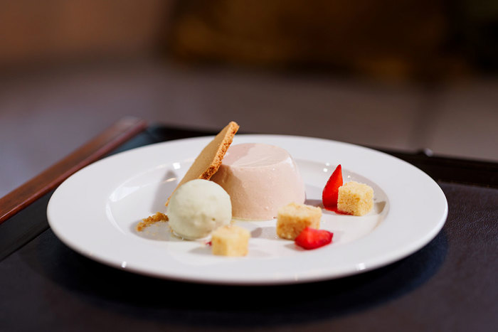 Elegantly plated dessert featuring a smooth panna cotta, complemented by a scoop of refreshing sorbet, delicate pieces of cake, and a crispy wafer cookie, served with artful touches