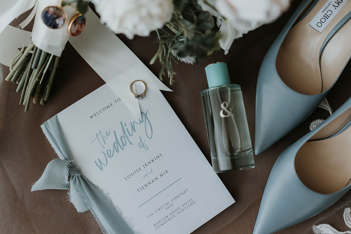 Flat lay of wedding details including invitation, engagement ring, bouquet, Jimmy Choo shoes and perfume 