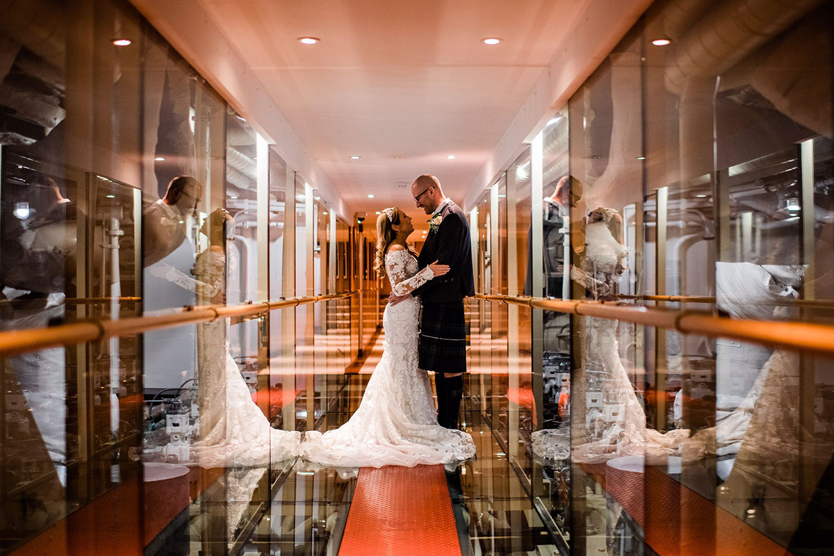 Newlyweds standing in Fingal’s glass-walled Engine Room corridor, surrounded by reflections and soft amber lighting