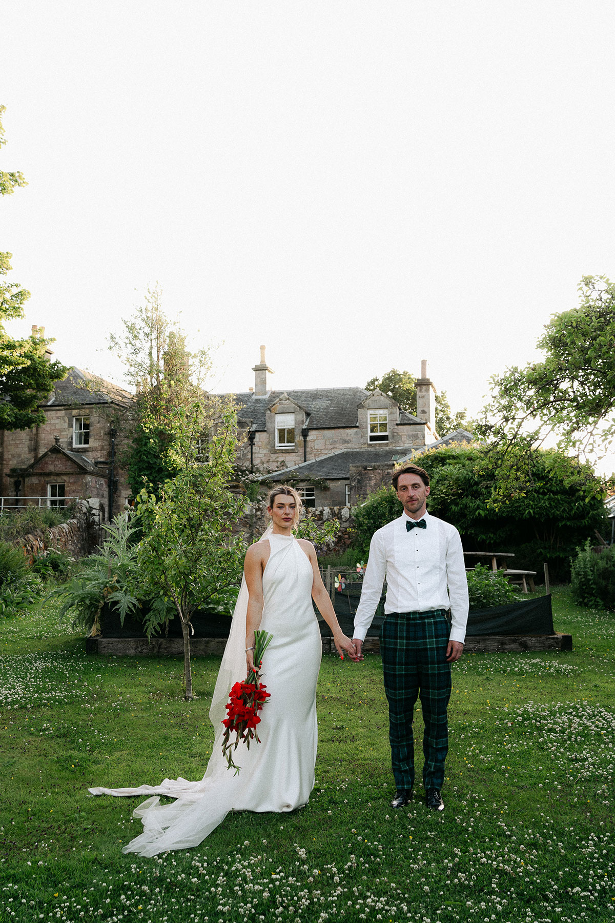 Bride and groom hold hands in Kinkell Byre's garden at sunset.