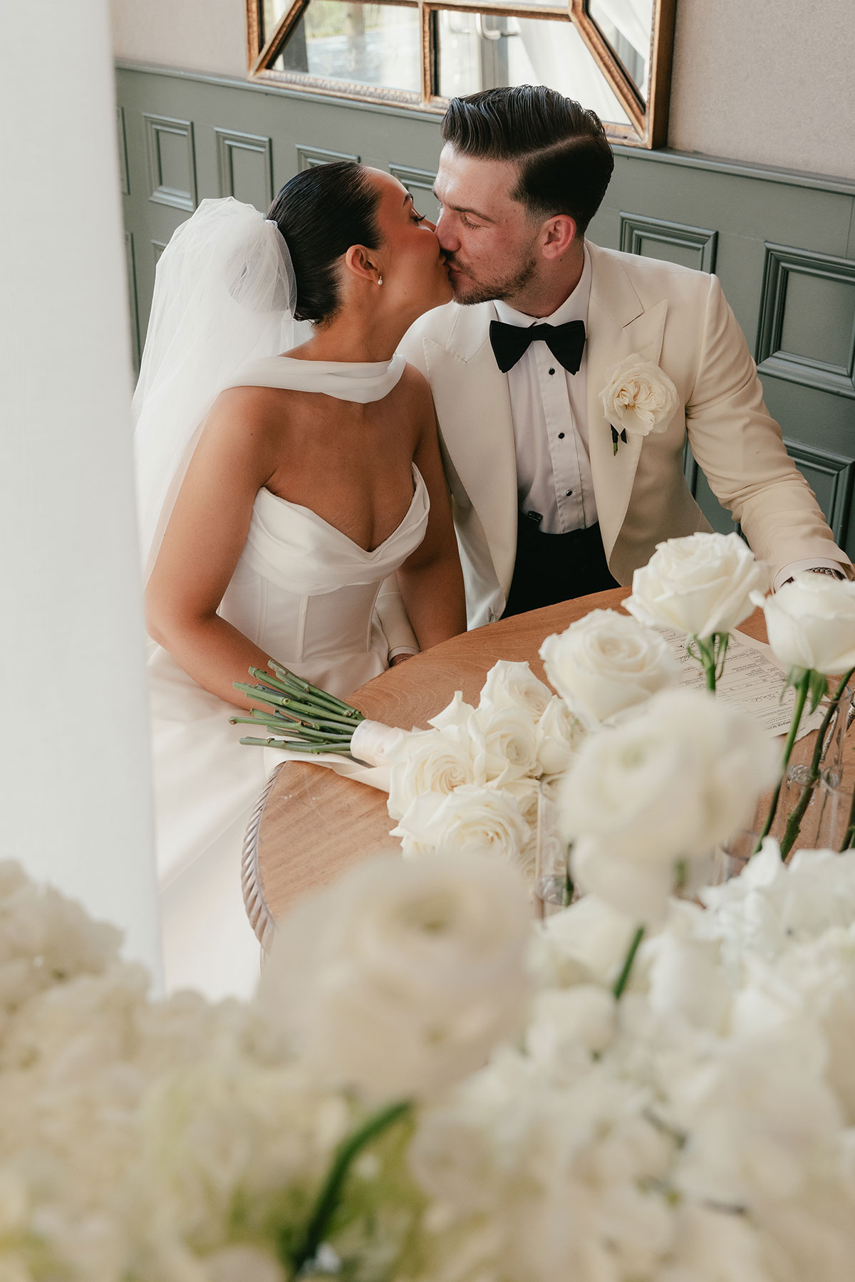 Bride and groom kissing while signing wedding register with white floral styling at Enterkine Country House