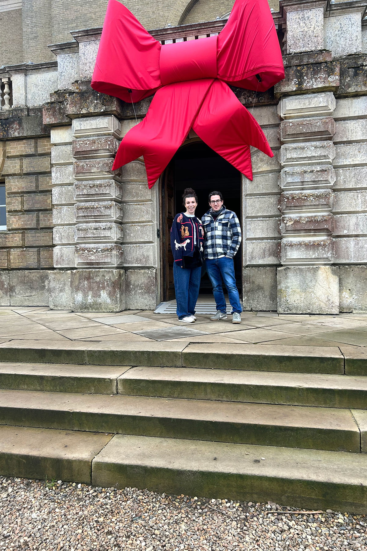 Couple standing on stone steps beneath a large red bow outside a historic Scottish building