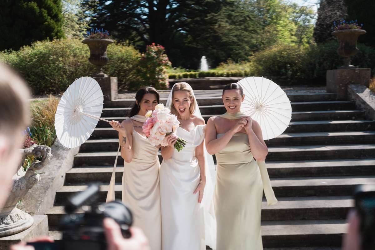Siân with her bridesmaids holding white parasols in the gardens at Mar Hall during her spring wedding in Renfrewshire.