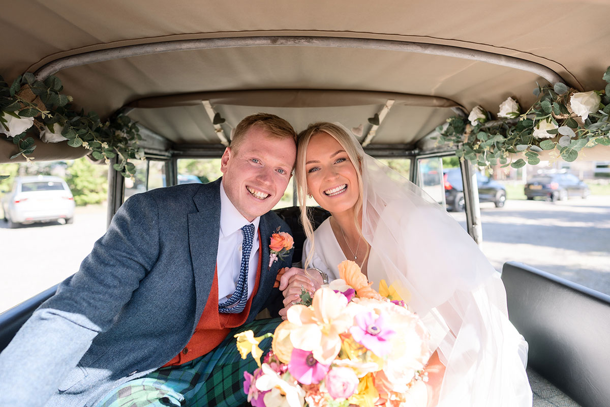 bride and groom hold hands and smile inside a car on their wedding day at achnagairn castle