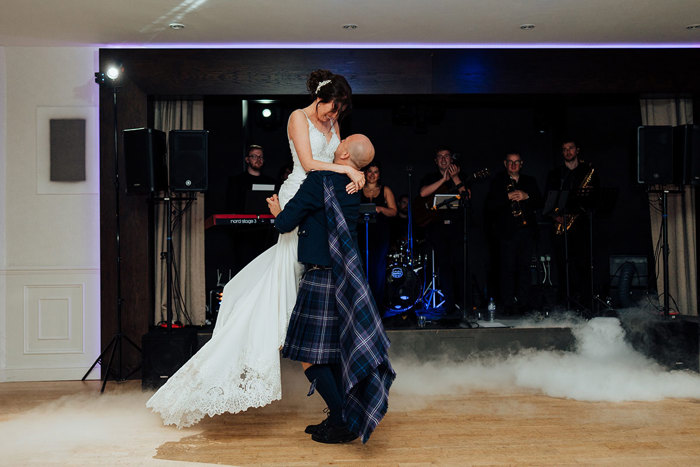 a groom lifts a bride up on the wooden dance floor at Seamill Hydro as a band performs in the background