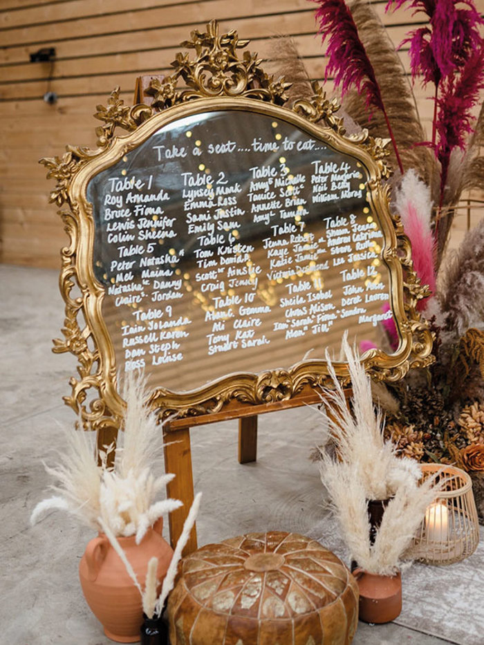 gold ornate mirror with white writing across it and an assortment of vases and candles placed at the base