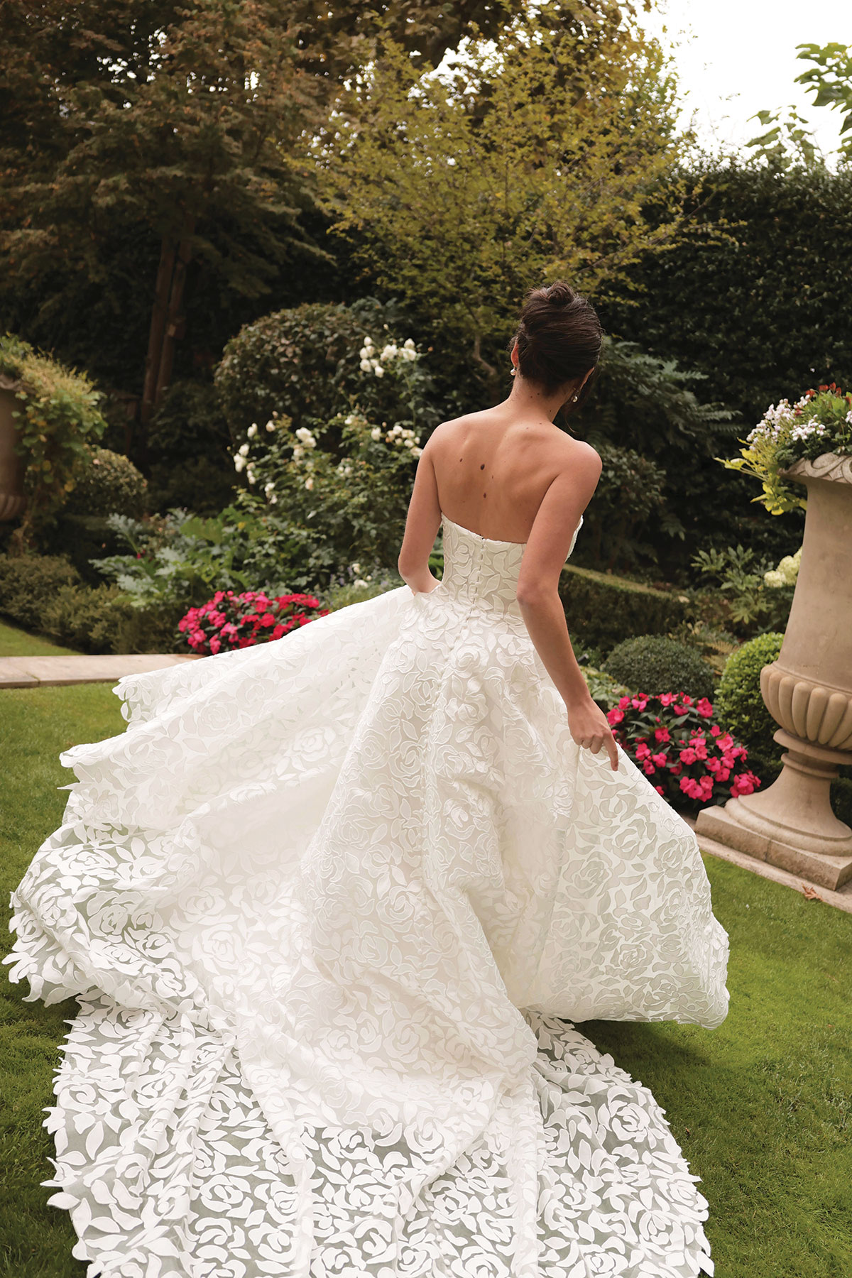 Bride wearing a strapless wedding dress with a voluminous floral appliqué skirt and train in a garden.