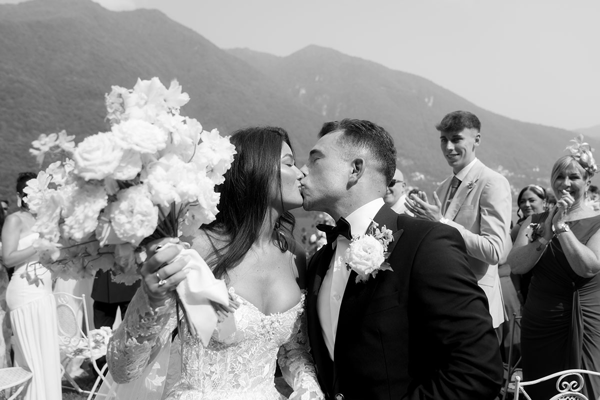 Bride and groom sharing a kiss after their Lake Como wedding ceremony, surrounded by guests and mountain views.