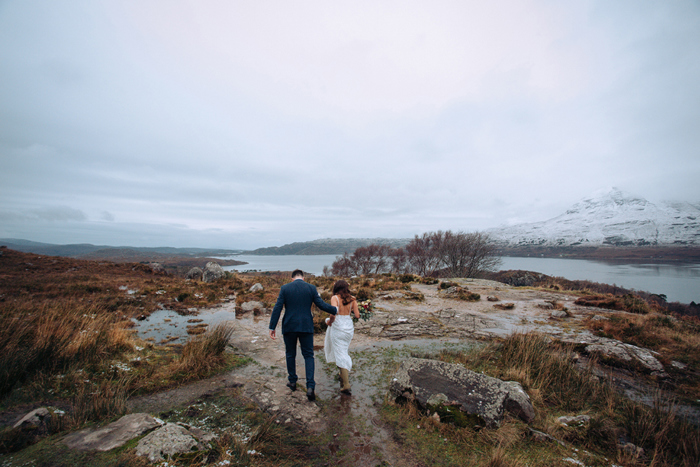 Bride and groom walk across ground with breathtaking highland scenery