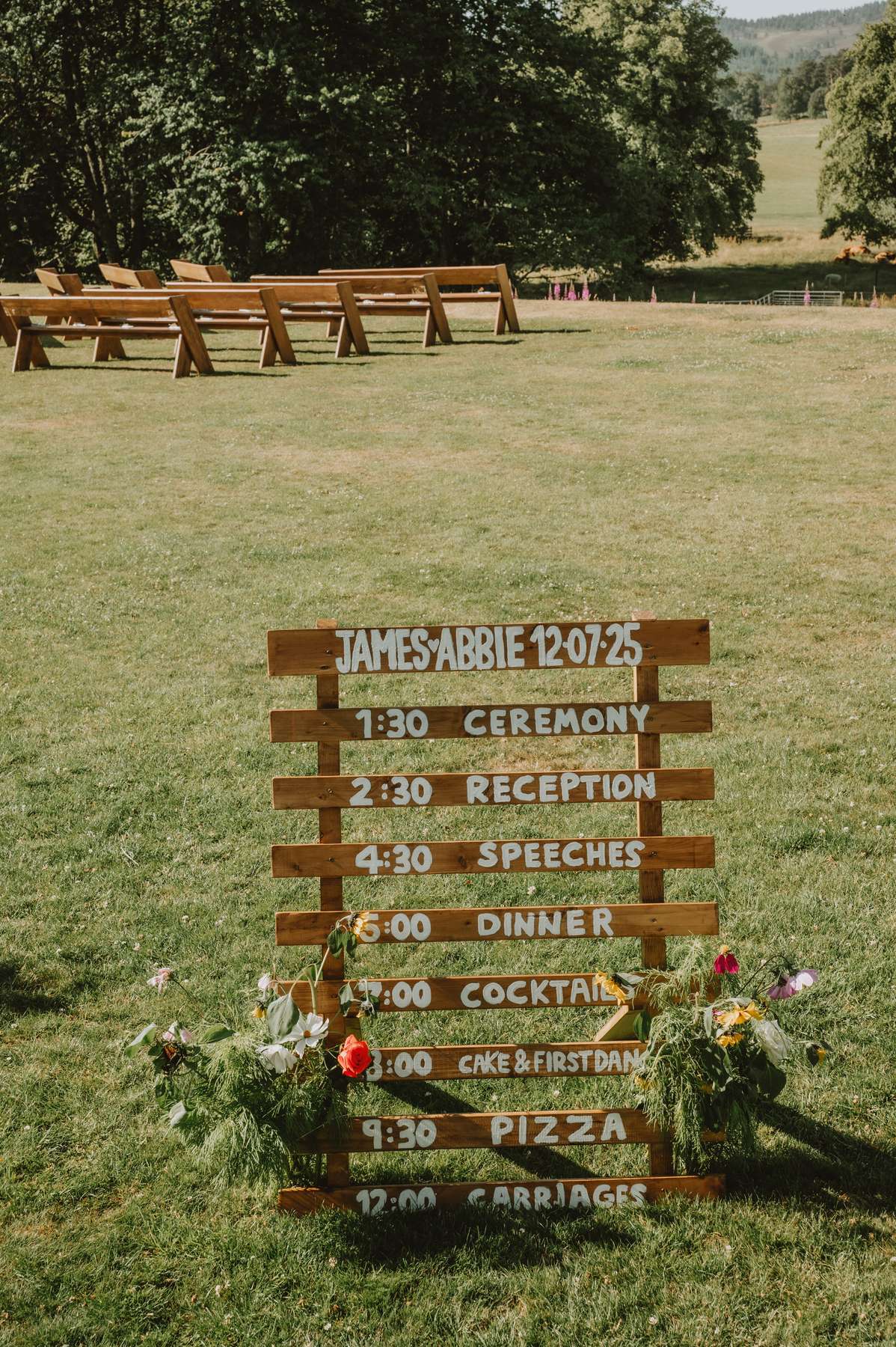 Rustic wooden wedding order-of-day sign beside outdoor ceremony benches at Ballogie House