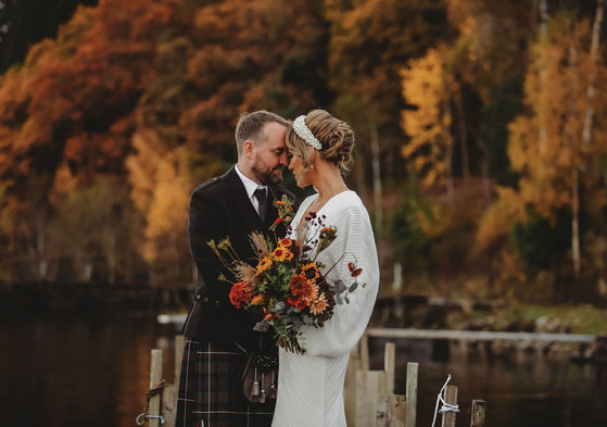 a bride and groom standing head to head with autumn trees turning gold and russet in background