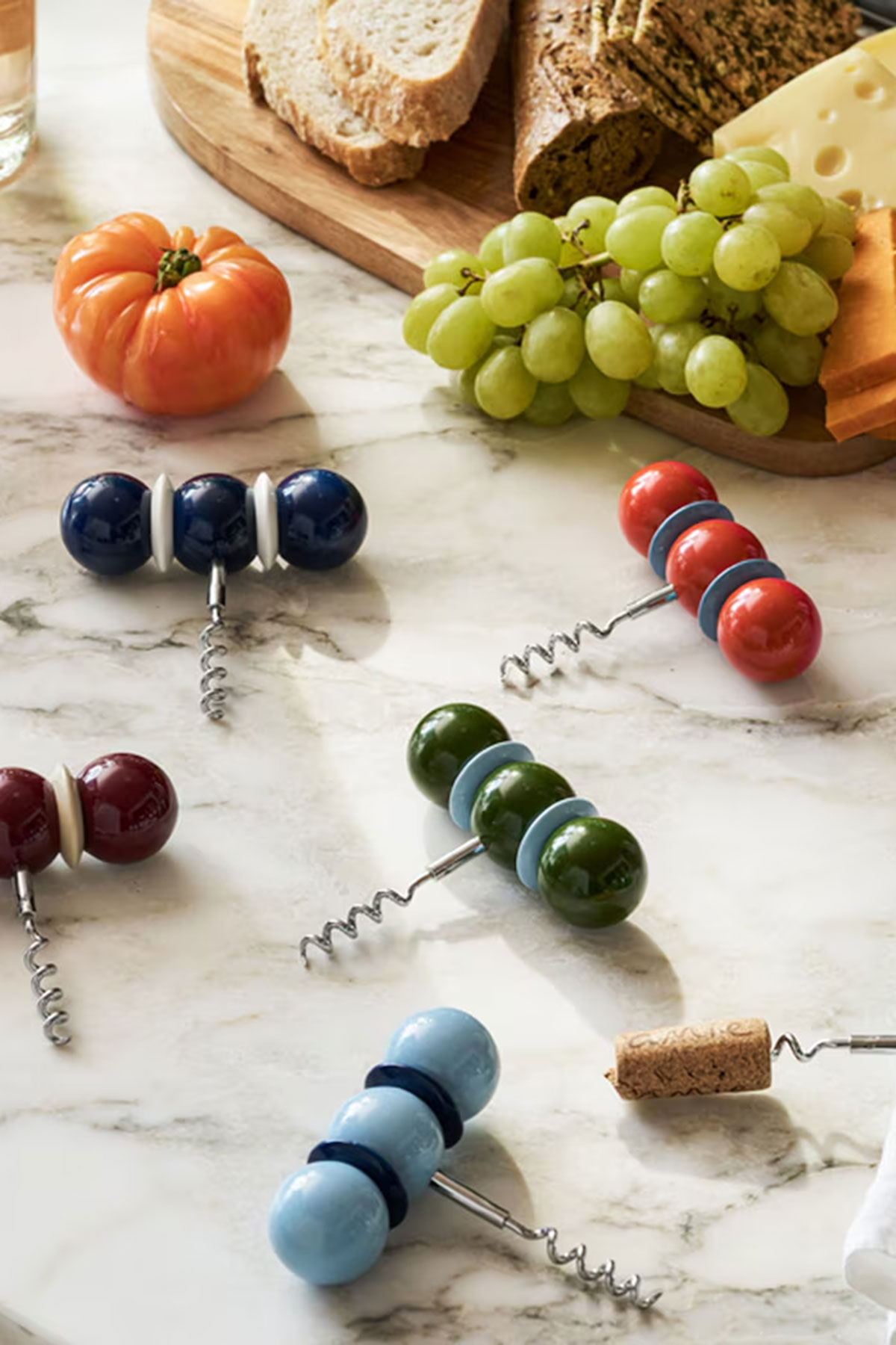 Colourful Addison Ross bobbin corkscrews styled with bread, cheese, grapes and tomato, a playful wedding gift idea for couples who love hosting