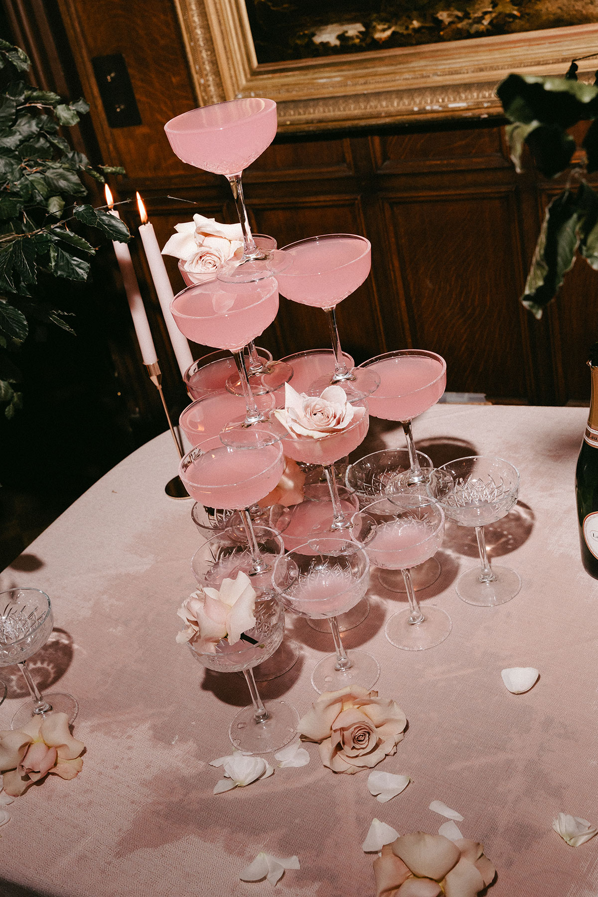Close-up view of a pink cocktail tower decorated with pale rose petals on a blush tablecloth