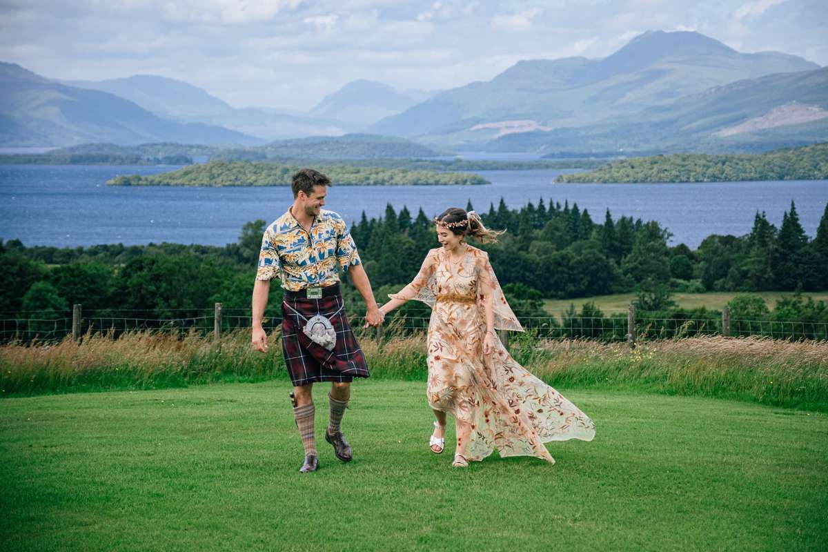 Newlyweds walking together on the lawn at Ardoch Loch Lomond overlooking the water and mountains