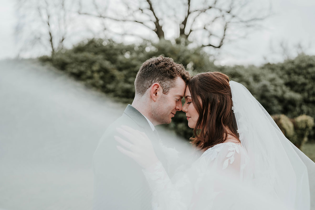 Portrait with the couple’s foreheads pressed together, veil creating a soft frame