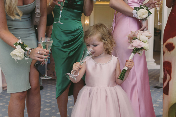 Little flower girl takes drink from champagne glass
