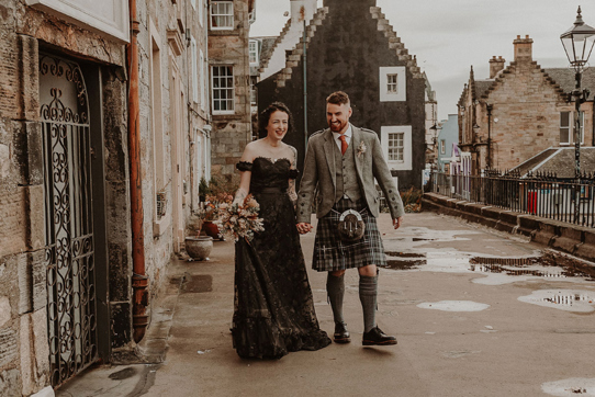 Couple walk holding hands on street in South Queensferry with bride in black wedding dress