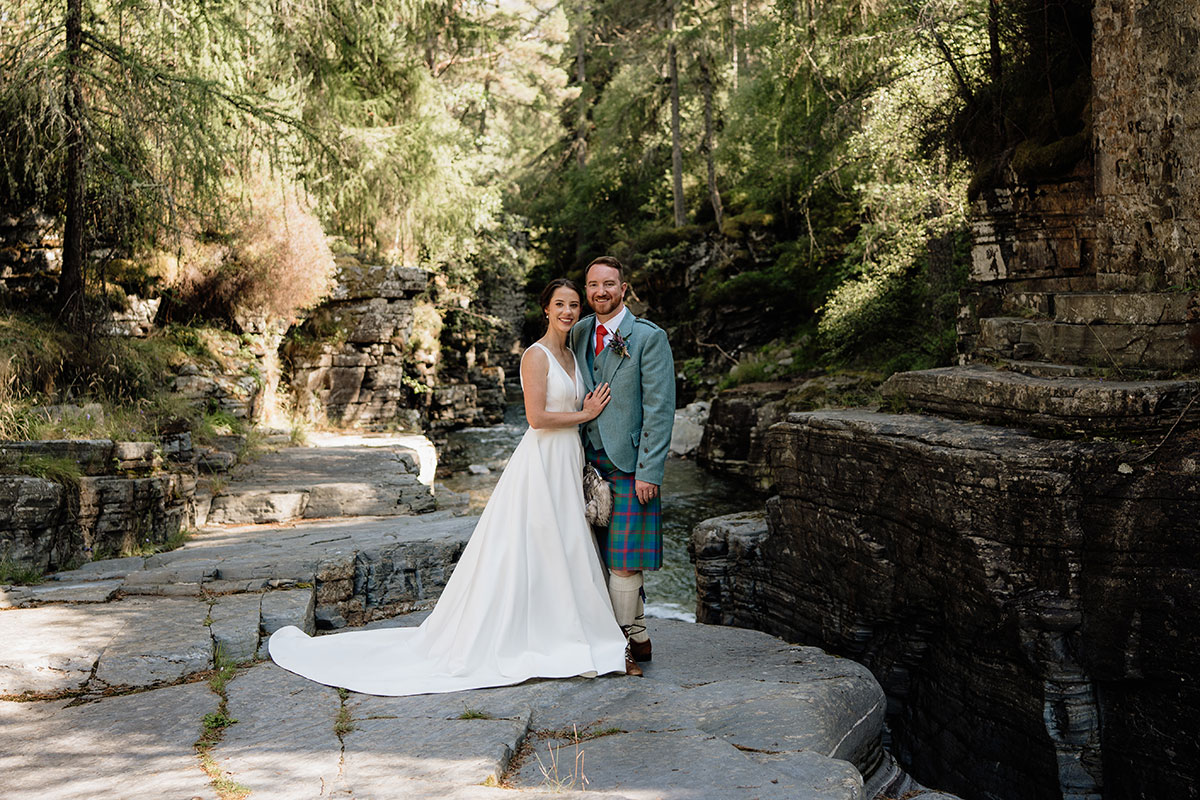 Bride and groom posing beside historic stone ruins and a river during wedding portraits in the Cairngorms National Park