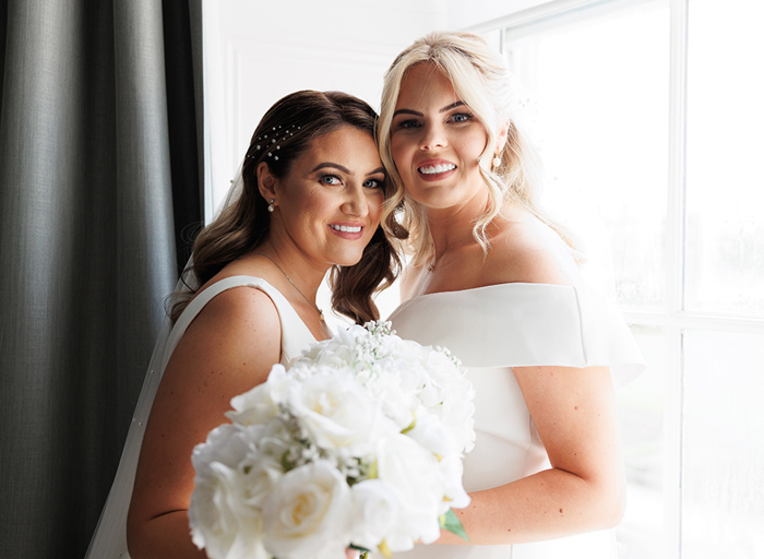 two brides smile while holding white floral wedding bouquets