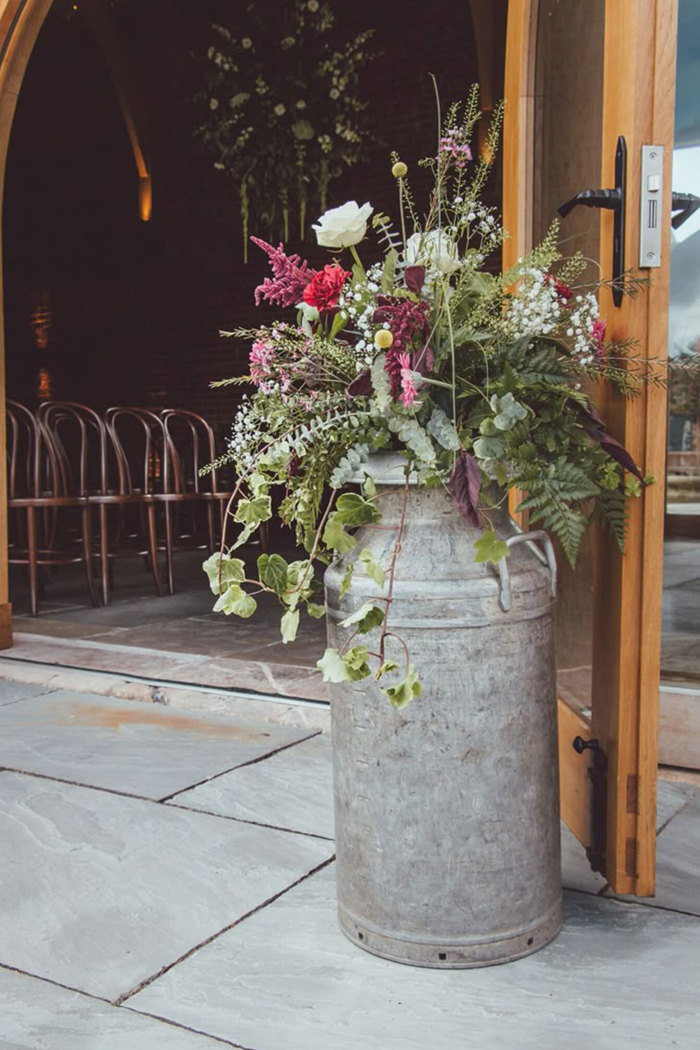 a metal milk churn with red and purple flowers in it