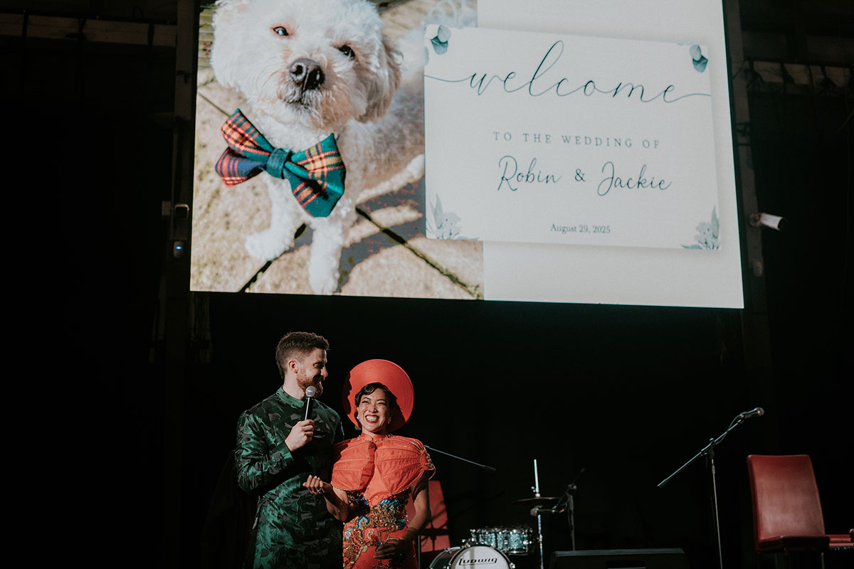 Bride and groom on stage during reception with wedding welcome screen and dog image at BAaD Glasgow