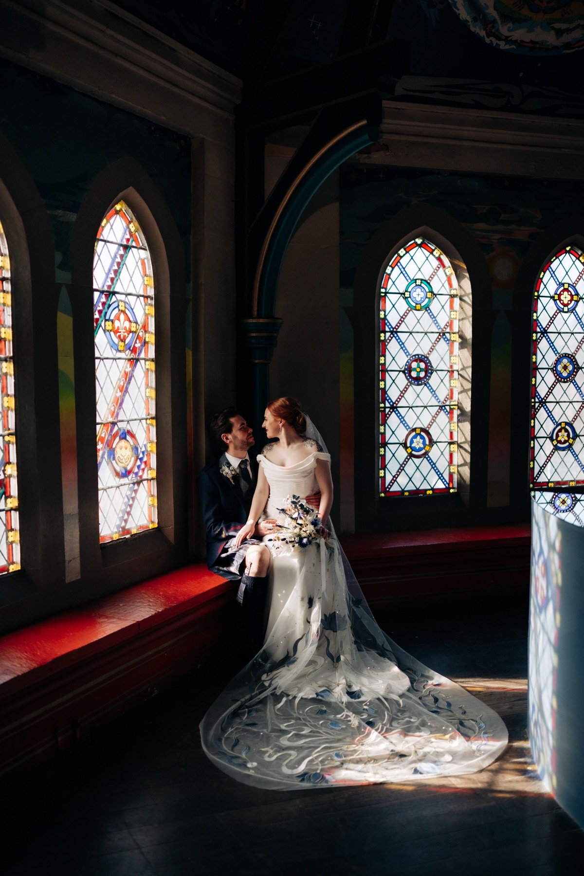 Robyn and James share a romantic wedding portrait beside the stained-glass windows at Òran Mór in Glasgow, showing Robyn's embroidered bridal veil.