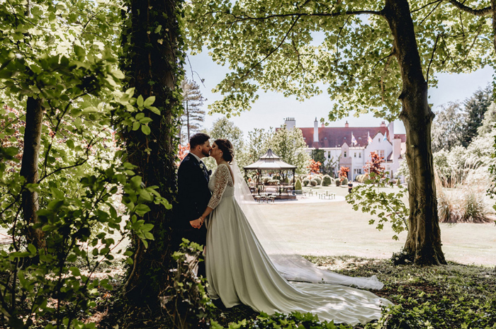 Bride and groom kiss under a tree in the grounds of Lochgreen House