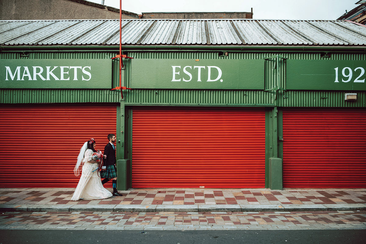 Wedding couple walking past the iconic Barras Market shutters in Glasgow East End near BAaD wedding venue