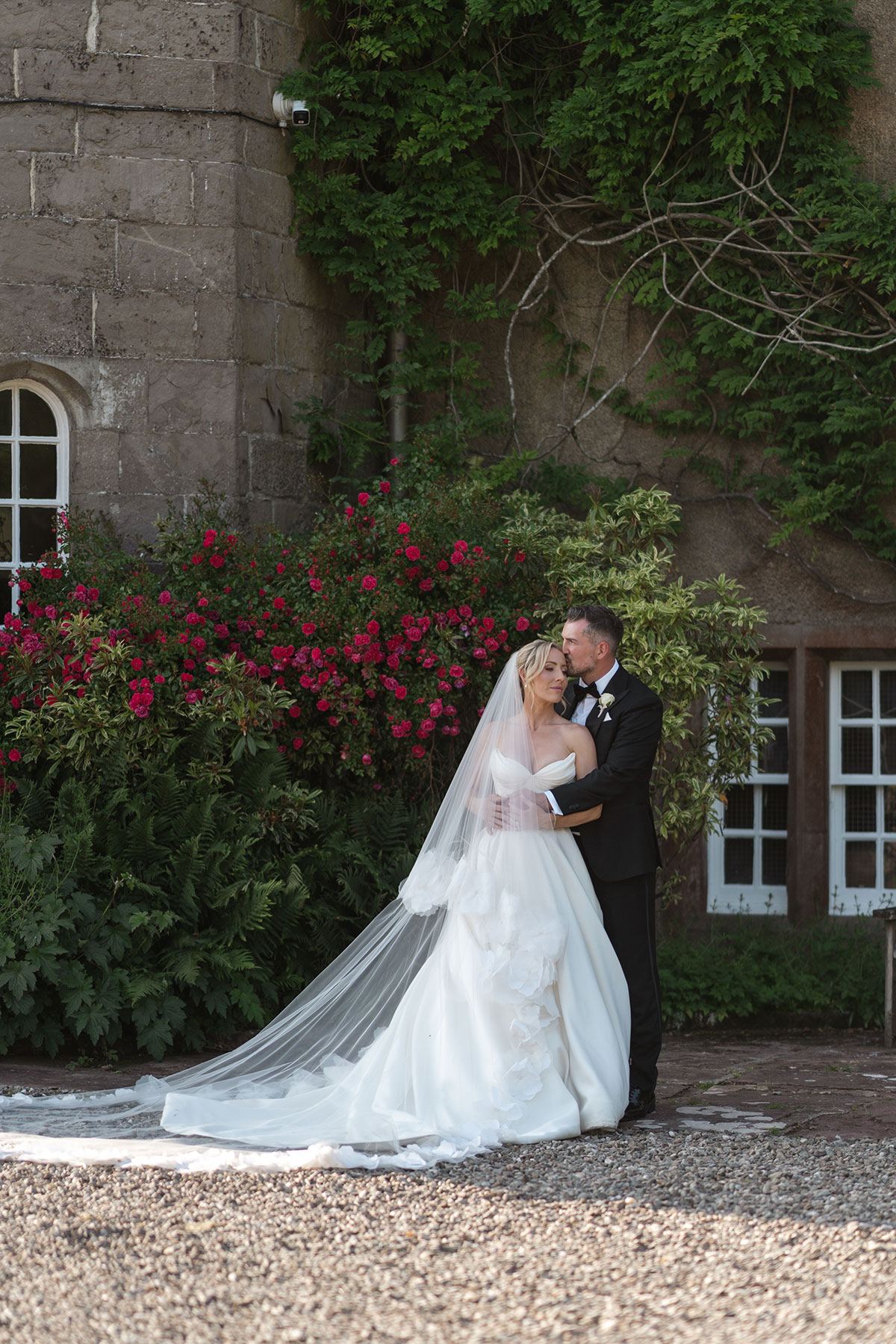 Bride and groom embrace outside Boturich Castle surrounded by colourful gardens after their Loch Lomond wedding ceremony.