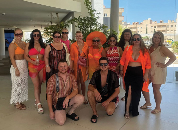 a group of people wearing orange and coral-toned beach and summer clothes posing for a photo in a glass-fronted room