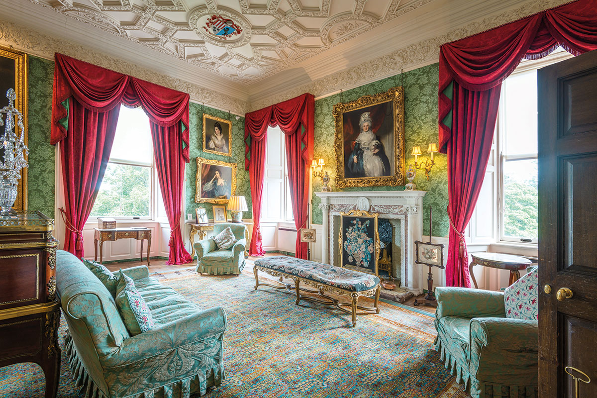 Drawing Room at Fyvie Castle with green damask walls, red curtains, antique furniture, portraits and ornate ceiling
