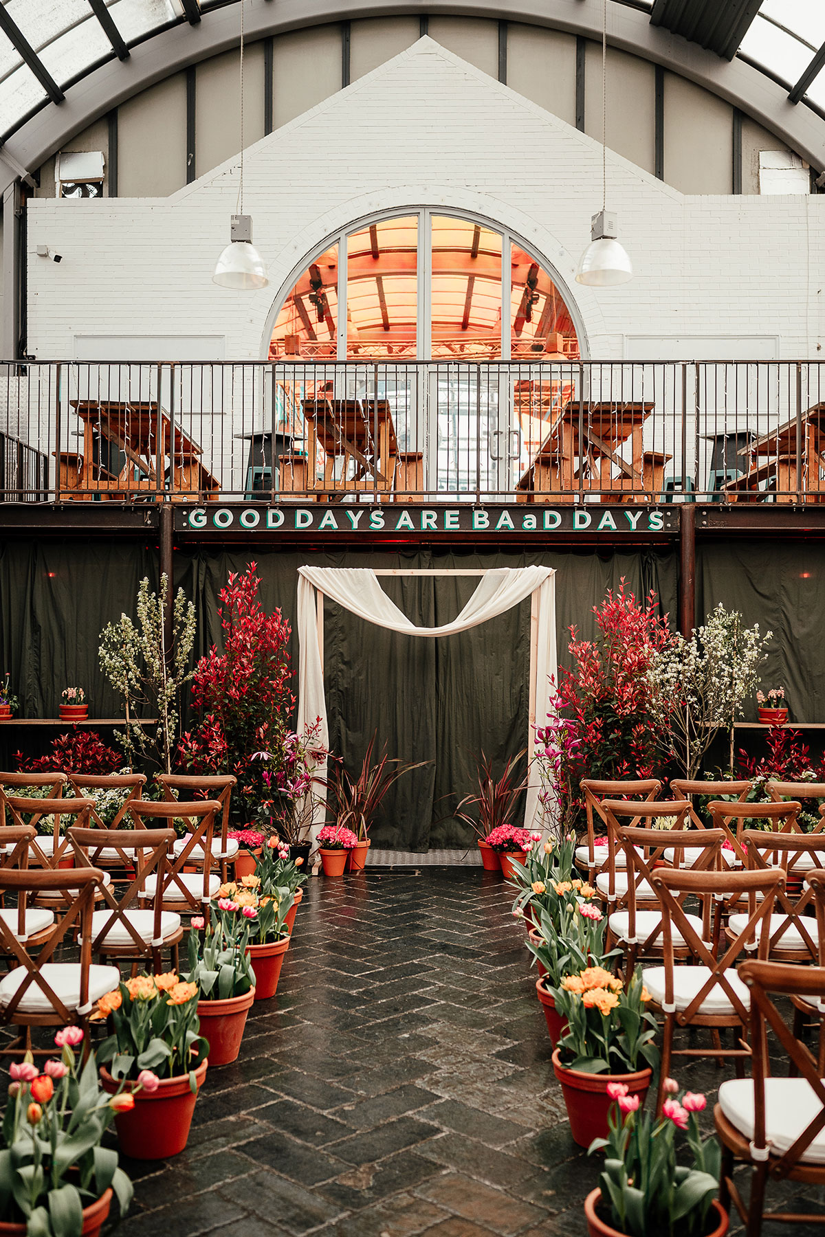 BAaD colourful wedding ceremony set up with wooden chairs and plant pots down aisle.