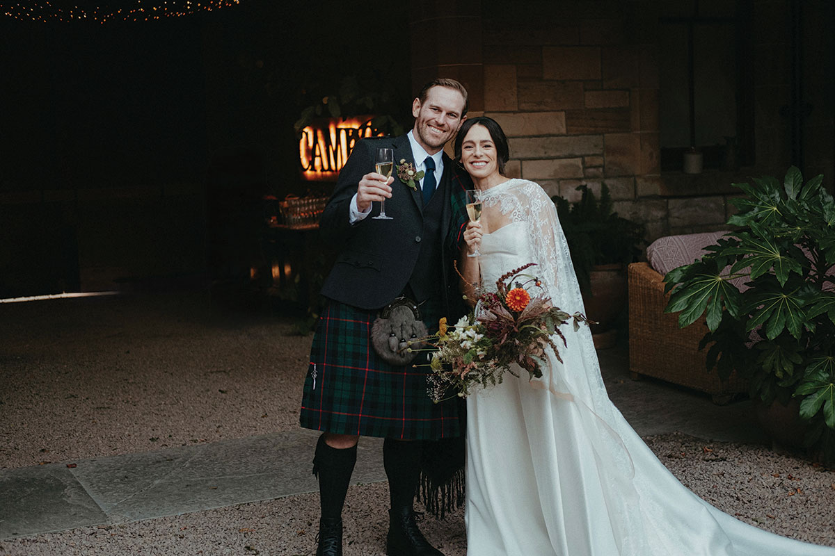 Newlyweds raise glasses of champagne and celebrate together in the courtyard at Cambo Country House following their wedding ceremony.