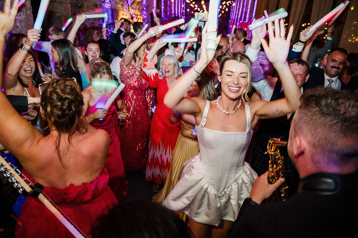 Bride dances on a packed dancefloor surrounded by guests waving glow sticks during the evening reception at Kinkell Byre in St Andrews.