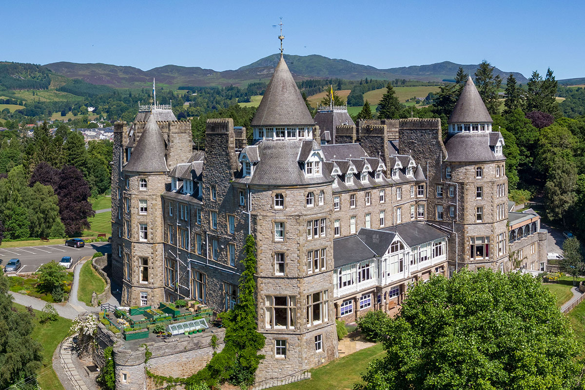 Aerial view of Atholl Palace Hotel in Pitlochry, showcasing the Victorian castle-style building set against the Perthshire countryside and hills