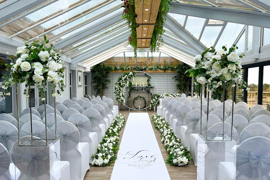 white ceremony room decorated with white aisle runner and white and green florals