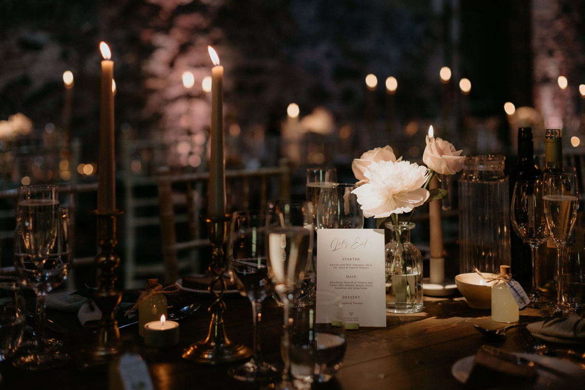 Wedding table setting at The Byre at Inchyra with candles, pale flowers, glassware and printed menu.