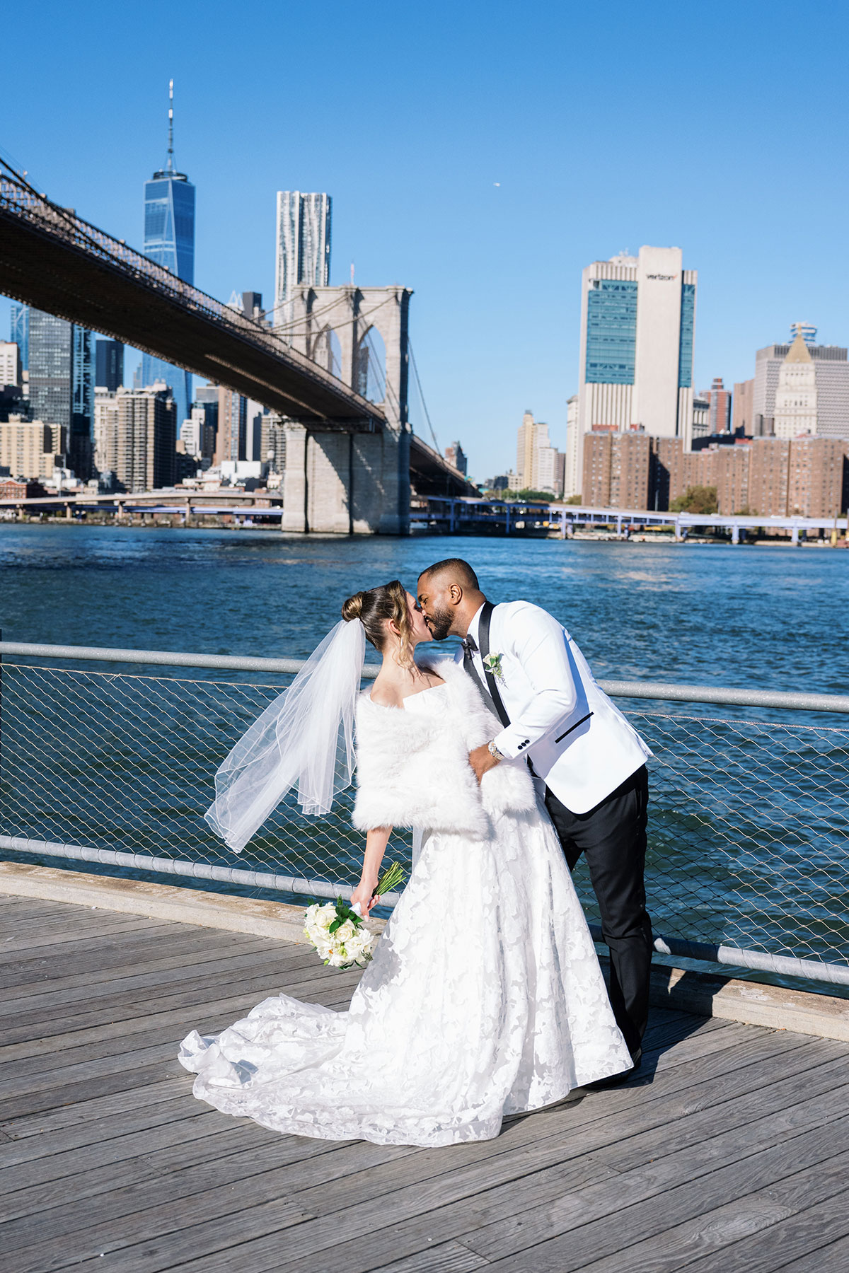 Couple kissing beside the waterfront with Brooklyn Bridge and Manhattan skyline in the background on a clear day