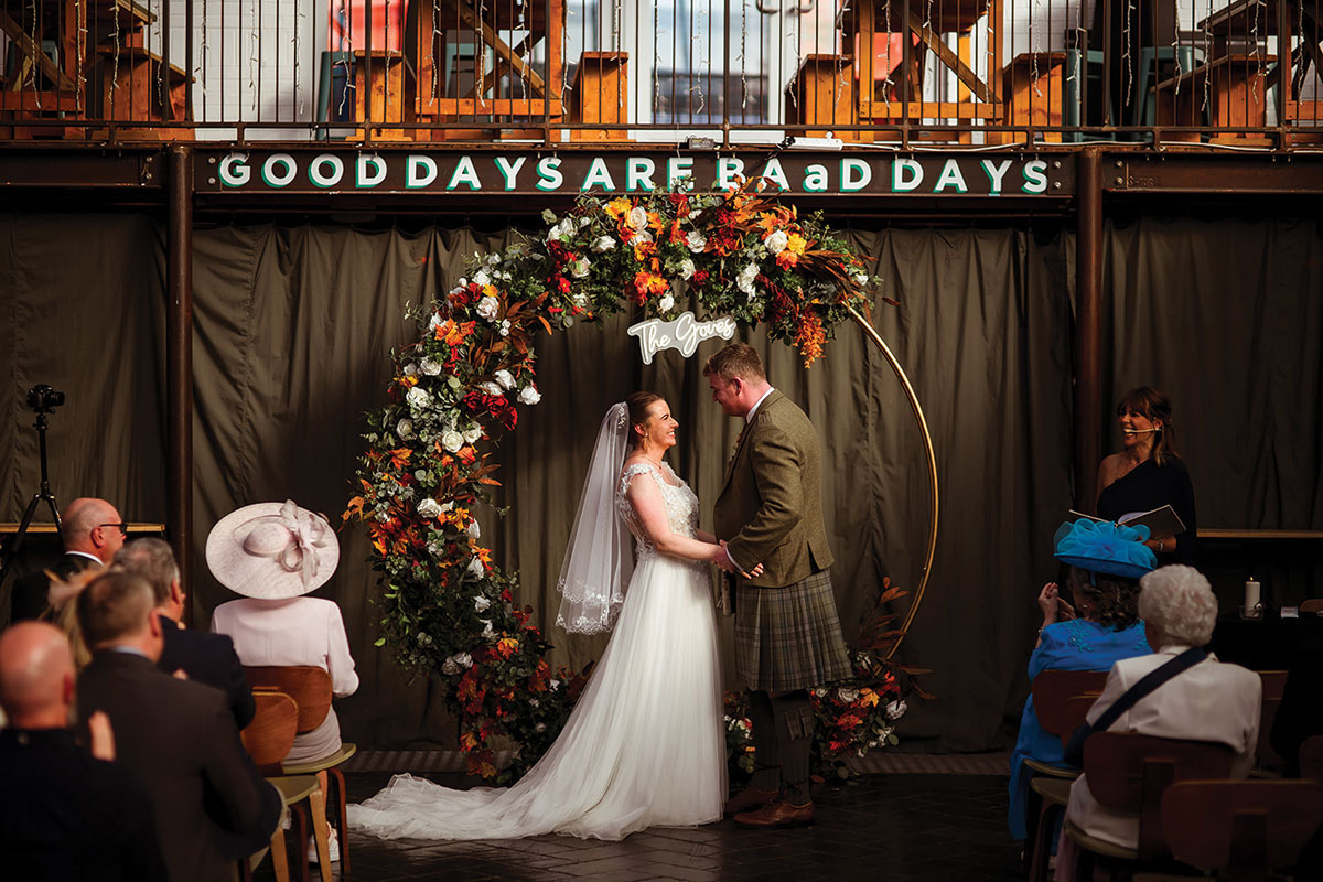 Bride and groom exchanging vows under a floral arch during a wedding ceremony at BAaD Glasgow in the Barras
