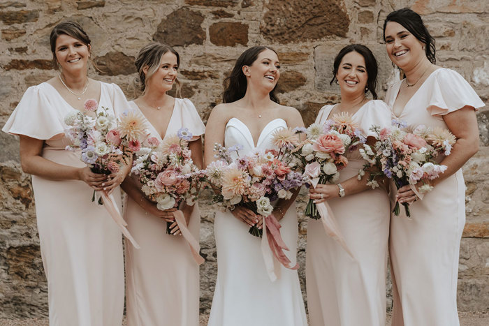 bride stands with her bridesmaids with pastel toned bouquets