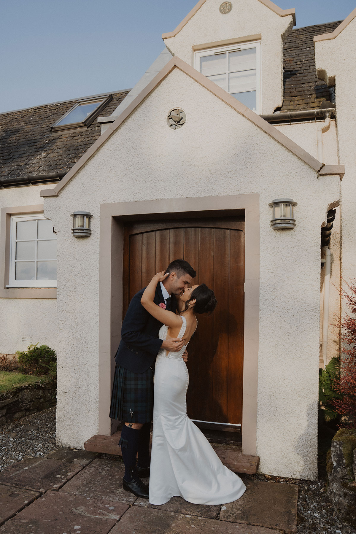 Newlyweds embracing outside cream country house wedding venue with wooden arched doorway in Scotland