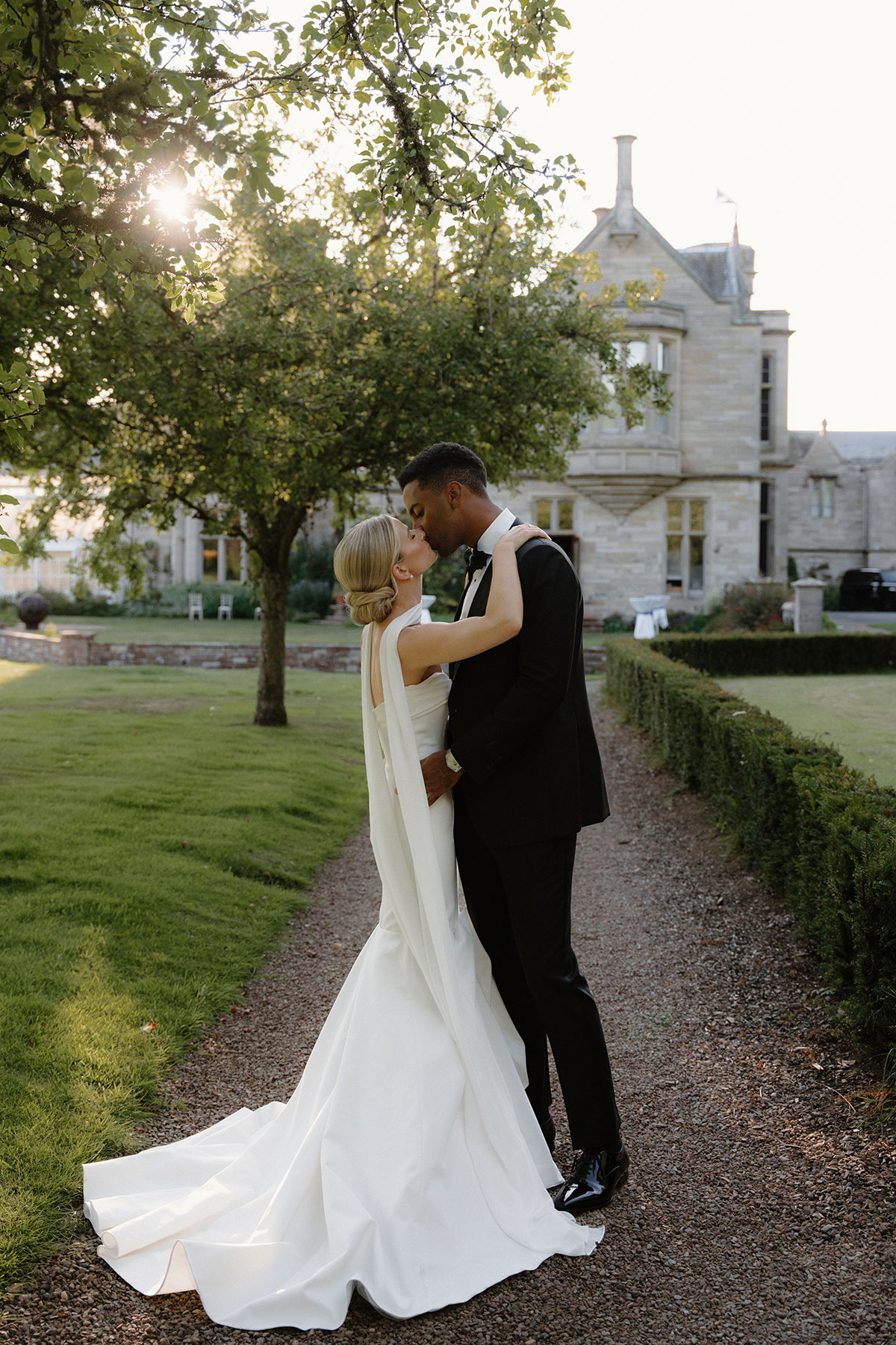 Romantic sunset wedding portrait of the couple kissing on a gravel pathway outside a Scottish castle wedding venue