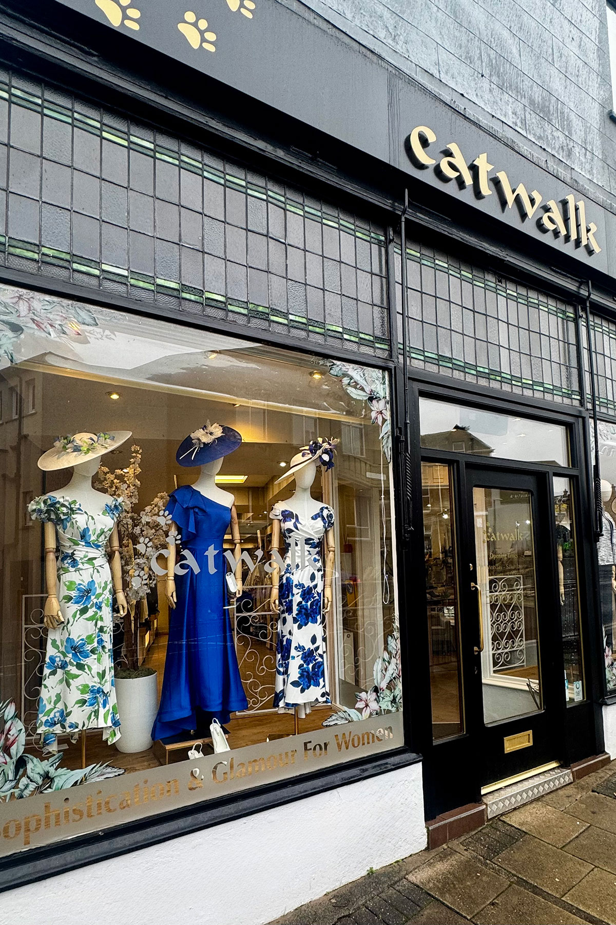Exterior of Catwalk boutique showing window display of mannequins in elegant blue and floral dresses, with the shop name above the entrance